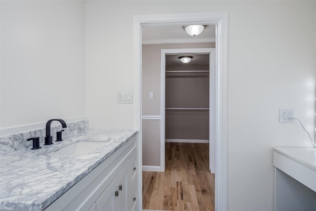 bathroom featuring baseboards, wood finished floors, vanity, and crown molding