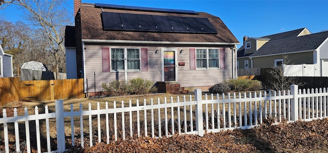 colonial inspired home with solar panels, a fenced front yard, and roof with shingles