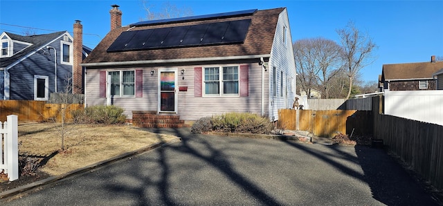 view of front of property with fence, entry steps, roof with shingles, roof mounted solar panels, and a chimney