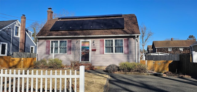 dutch colonial featuring a fenced front yard, roof mounted solar panels, and a shingled roof