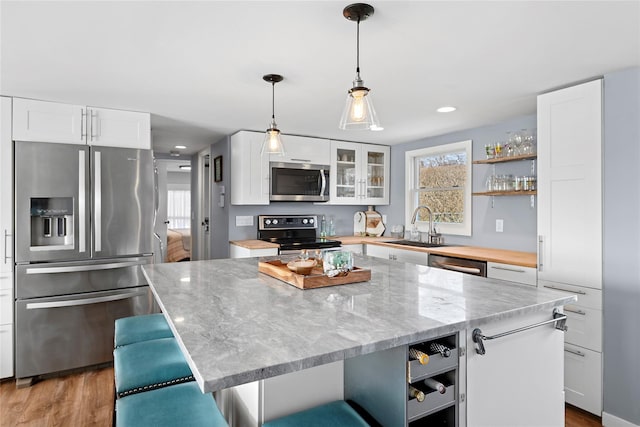 kitchen featuring a kitchen island, open shelves, a sink, white cabinets, and appliances with stainless steel finishes