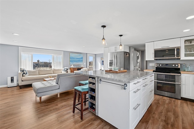 kitchen featuring open floor plan, dark wood-style floors, white cabinets, stainless steel appliances, and stacked washer / drying machine