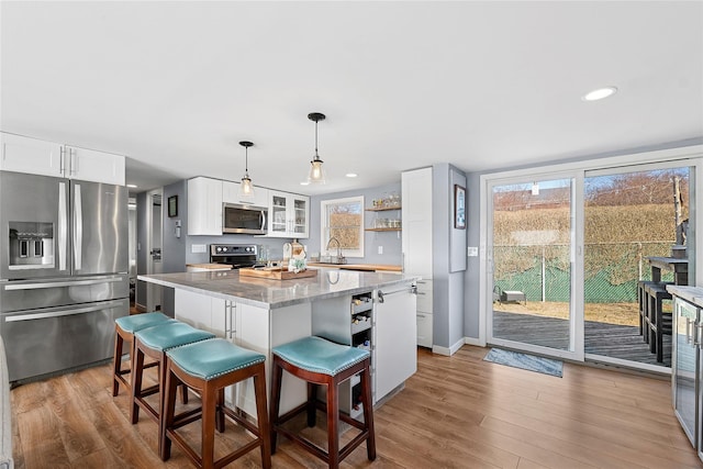 kitchen featuring open shelves, stainless steel appliances, light wood-style floors, and a center island