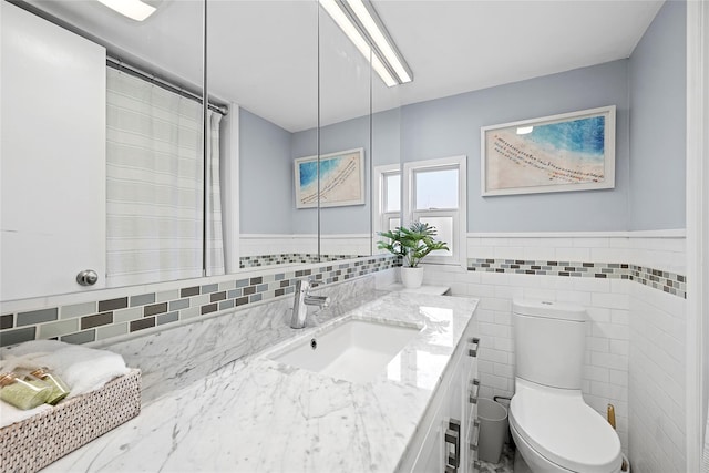 bathroom with vanity, tile walls, toilet, and wainscoting