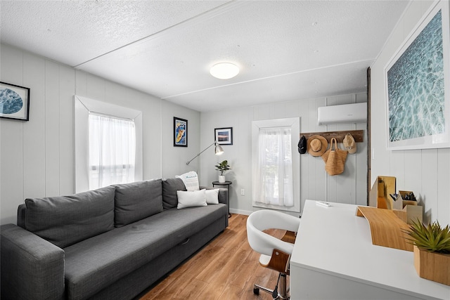 living room featuring a wealth of natural light, a textured ceiling, a wall mounted air conditioner, and light wood-type flooring