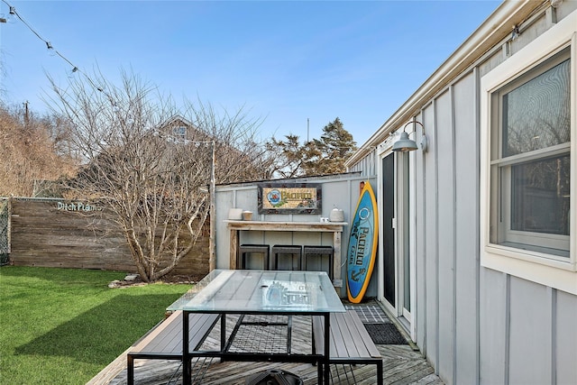 wooden terrace with outdoor dining space, fence, and a lawn