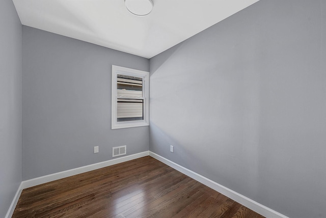 empty room featuring dark wood-style floors, visible vents, and baseboards