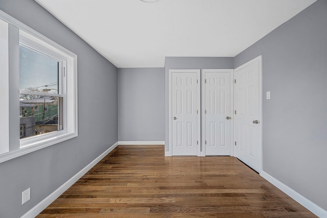 unfurnished bedroom featuring baseboards, wood finished floors, and multiple closets