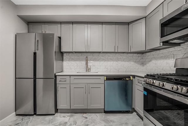 kitchen featuring gray cabinets, a sink, stainless steel appliances, light countertops, and decorative backsplash