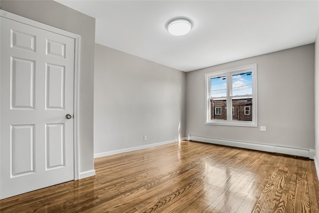 unfurnished room with a baseboard heating unit, baseboards, and wood finished floors