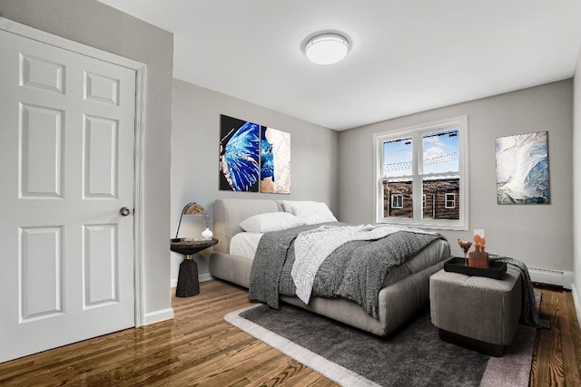 bedroom featuring a baseboard radiator, baseboards, and wood finished floors