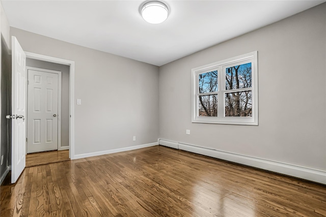 unfurnished room featuring baseboard heating, baseboards, and wood finished floors