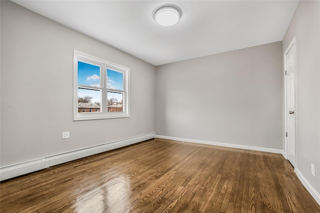 empty room featuring a baseboard heating unit, baseboards, and wood finished floors