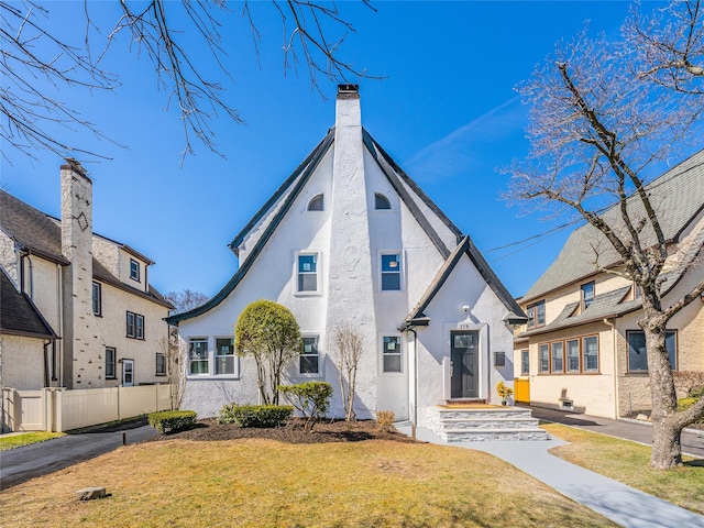 view of front of house with a front yard, fence, a chimney, and stucco siding