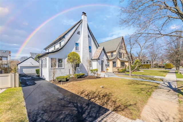 tudor home with a front lawn, fence, stucco siding, a garage, and an outdoor structure