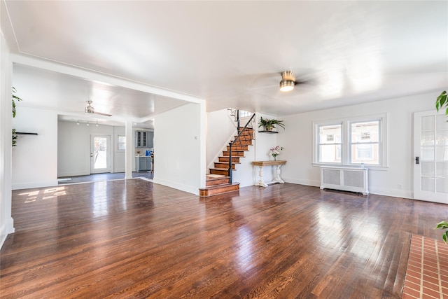 unfurnished living room with hardwood / wood-style floors, radiator, baseboards, ceiling fan, and stairs