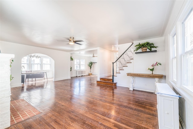 unfurnished living room featuring radiator, ceiling fan, stairs, wood finished floors, and arched walkways
