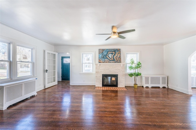 unfurnished living room with arched walkways, radiator, wood finished floors, and a ceiling fan