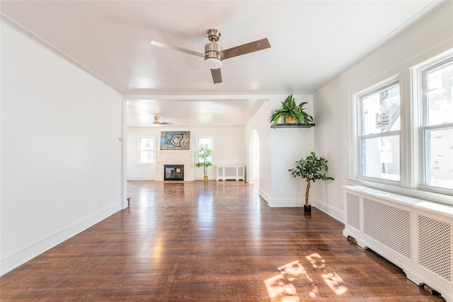 unfurnished living room with arched walkways, radiator, wood finished floors, and a ceiling fan