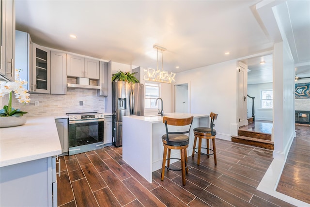 kitchen with wood finish floors, gray cabinets, tasteful backsplash, stainless steel appliances, and wall chimney exhaust hood