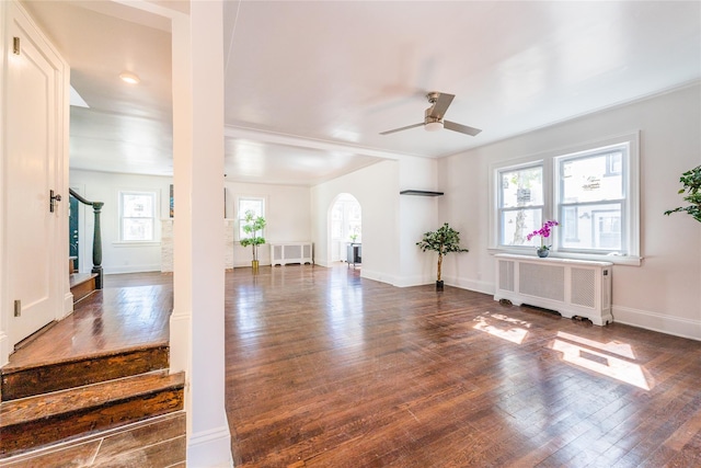 living area featuring arched walkways, dark wood finished floors, radiator heating unit, and ceiling fan