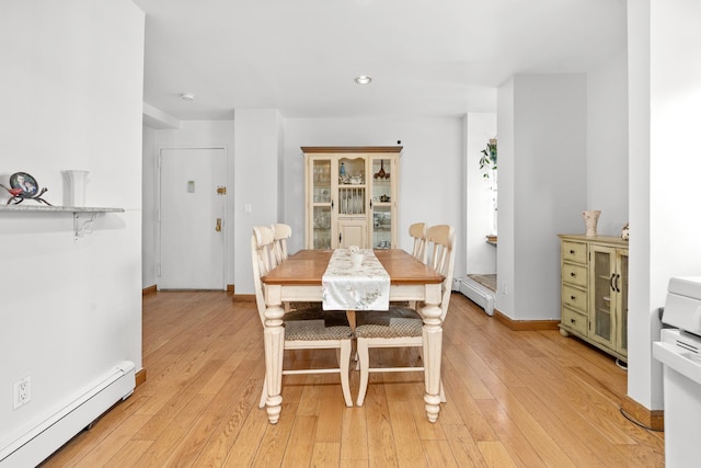 dining room featuring a baseboard radiator, baseboards, and light wood finished floors