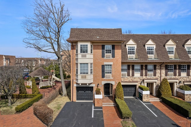 townhome / multi-family property featuring aphalt driveway, brick siding, roof with shingles, and a garage