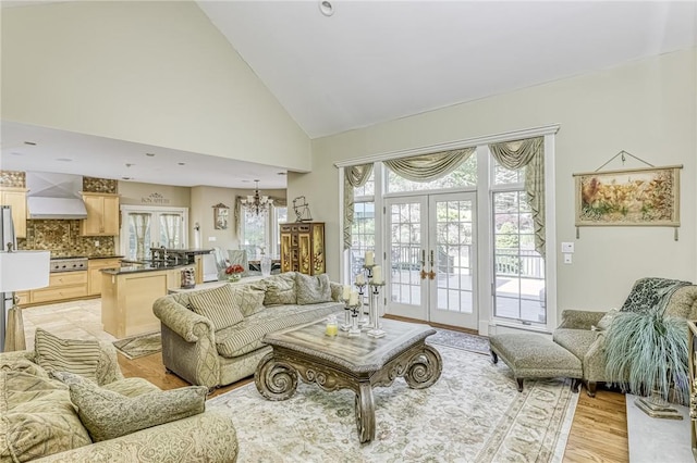 living room featuring light wood-type flooring, french doors, a notable chandelier, and high vaulted ceiling