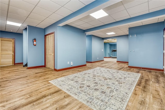 empty room featuring wood finished floors, baseboards, and a paneled ceiling