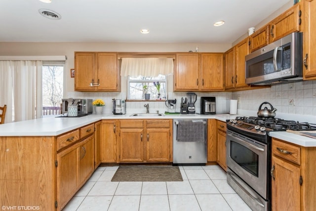 kitchen with light countertops, appliances with stainless steel finishes, a peninsula, plenty of natural light, and a sink