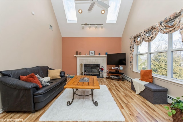 living room with a baseboard heating unit, a skylight, a ceiling fan, and light wood-type flooring