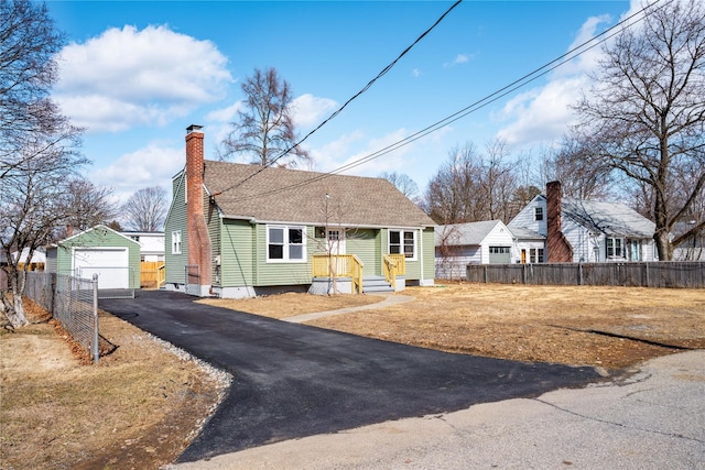 view of front of home with a detached garage, fence, aphalt driveway, a chimney, and an outbuilding