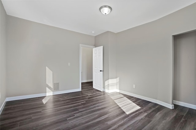 empty room featuring visible vents, baseboards, and dark wood finished floors