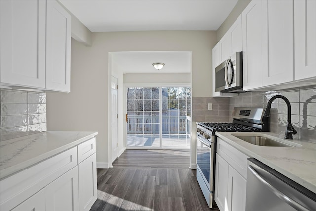 kitchen with dark wood-type flooring, a sink, white cabinetry, stainless steel appliances, and light stone countertops