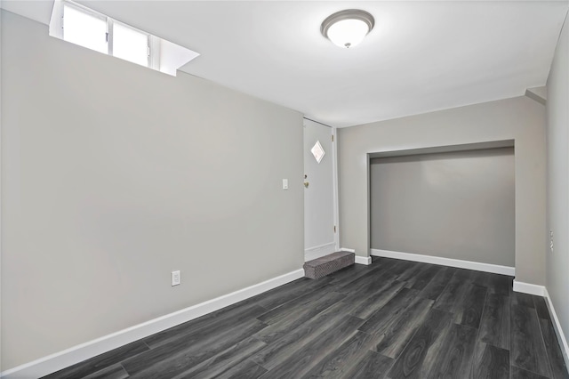 spare room with baseboards and dark wood-type flooring