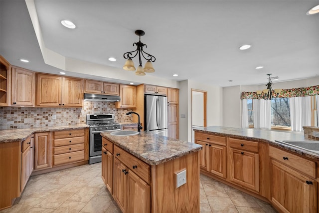 kitchen featuring a kitchen island with sink, under cabinet range hood, a sink, stainless steel appliances, and decorative backsplash