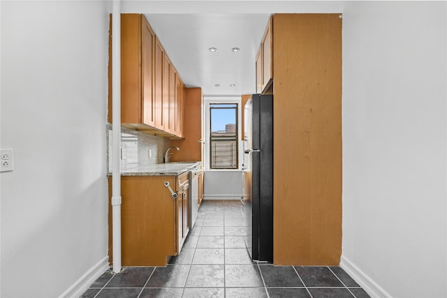 kitchen featuring tile patterned flooring, brown cabinetry, tasteful backsplash, and freestanding refrigerator