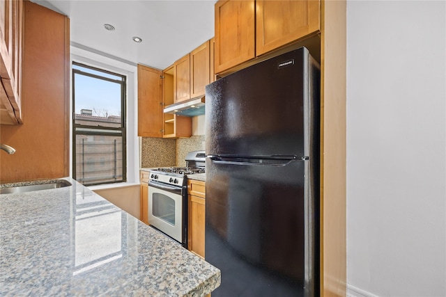 kitchen featuring a sink, under cabinet range hood, tasteful backsplash, freestanding refrigerator, and stainless steel range with gas cooktop