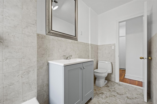 bathroom featuring toilet, tile walls, wainscoting, and vanity