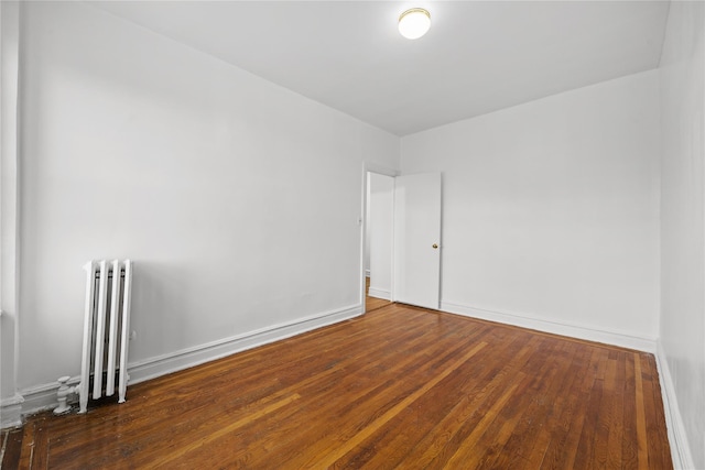 empty room featuring hardwood / wood-style floors, radiator heating unit, and baseboards