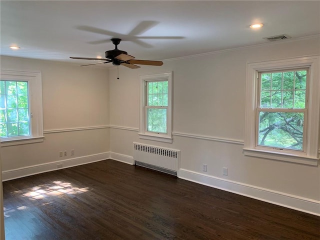 spare room featuring baseboards, dark wood-type flooring, radiator, and a healthy amount of sunlight