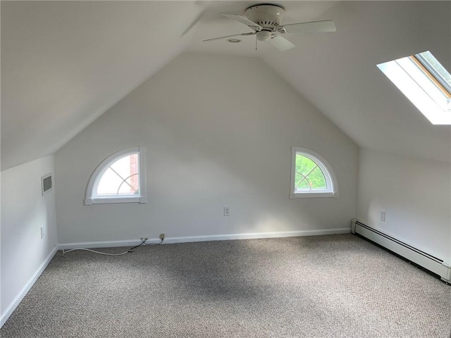 additional living space featuring a baseboard heating unit, vaulted ceiling with skylight, carpet, and a healthy amount of sunlight