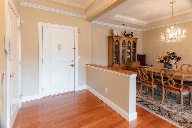 foyer with light wood finished floors, baseboards, ornamental molding, a notable chandelier, and a raised ceiling