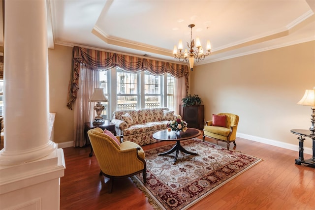 living area featuring wood finished floors, an inviting chandelier, decorative columns, crown molding, and a raised ceiling