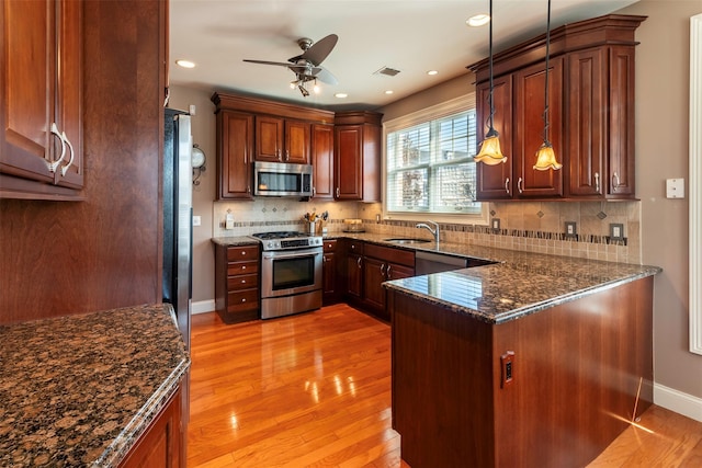 kitchen with dark stone counters, appliances with stainless steel finishes, light wood-style floors, a ceiling fan, and a sink