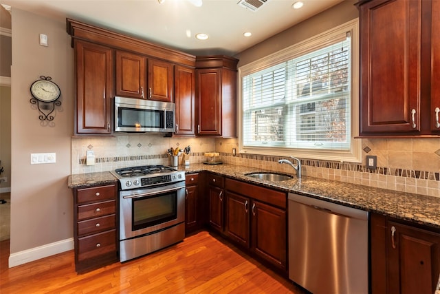 kitchen with baseboards, dark stone counters, light wood-style floors, stainless steel appliances, and a sink