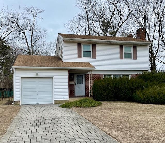 traditional home featuring an attached garage, a chimney, and driveway