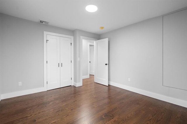 unfurnished bedroom featuring dark wood-style floors, visible vents, a closet, and baseboards