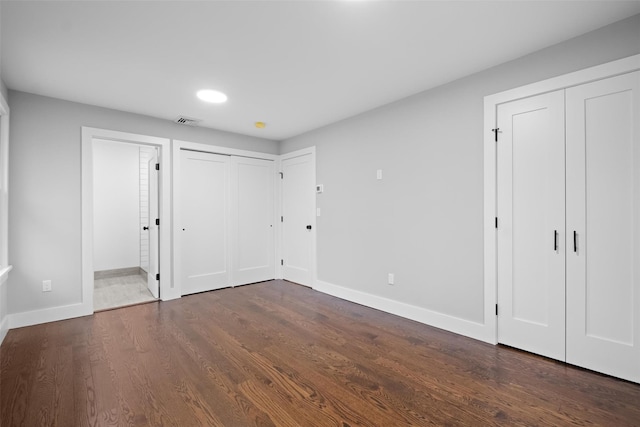 unfurnished bedroom featuring baseboards, visible vents, ensuite bath, dark wood-style flooring, and multiple closets