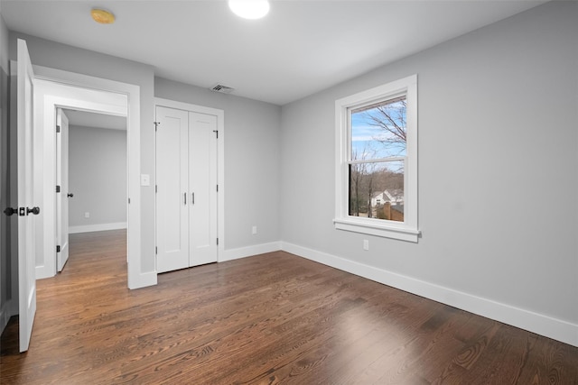 unfurnished bedroom featuring visible vents, baseboards, dark wood-type flooring, and a closet